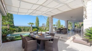 Un patio exterior con mobiliario de mimbre, piscina y vista al mar.