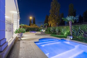 A swimming pool with a waterfall feature, surrounded by a landscaped garden with various plants and a seating area. - Luxury Lakefront Catullo A1 by Wonderful Italy (Sirmione)
