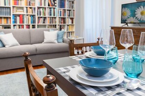 Un coin repas avec une table dressée pour quatre personnes, une bibliothèque en arrière-plan et un canapé au premier plan.