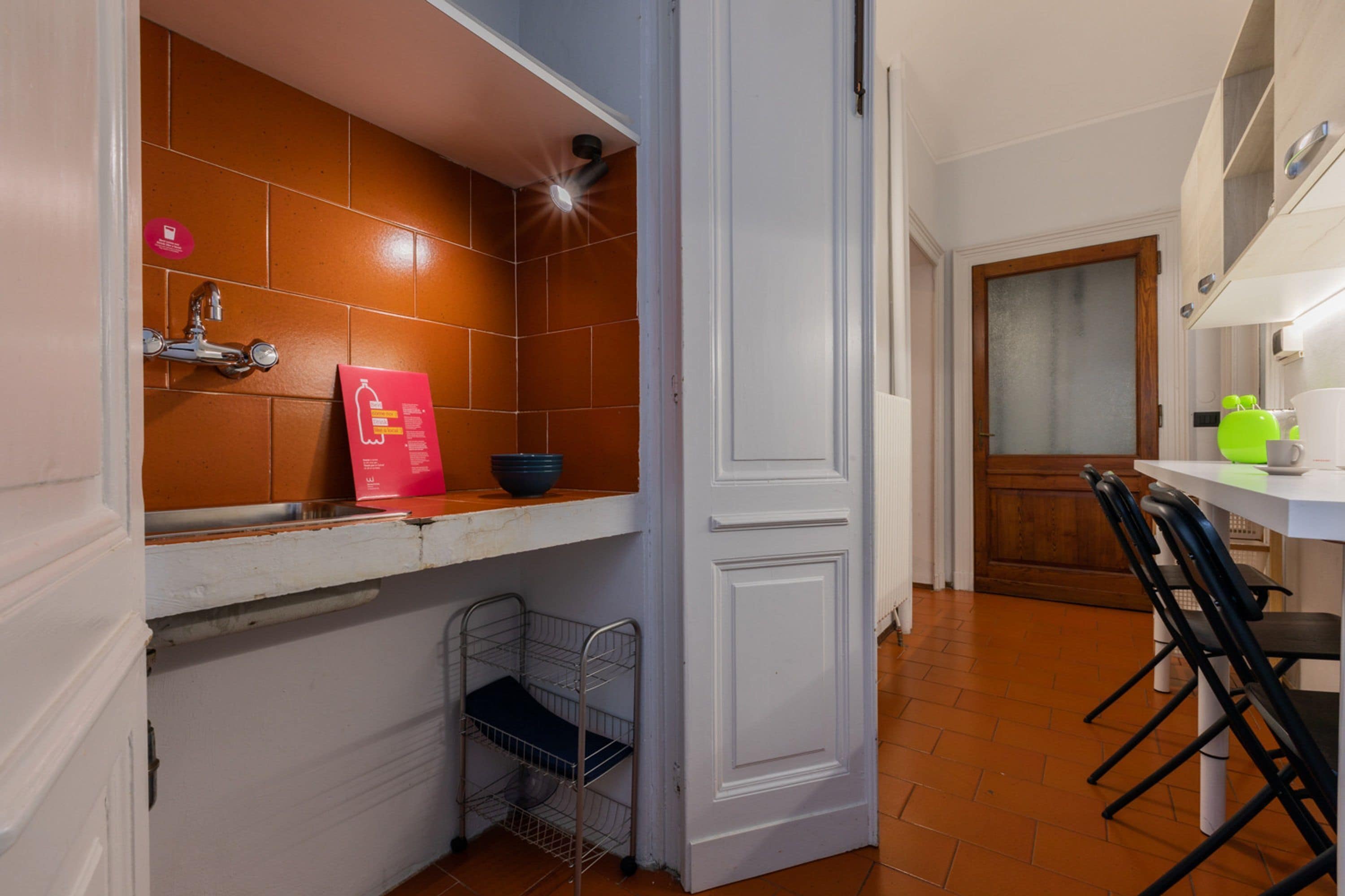 A kitchen with a white countertop, a sink, and a metal rack. There is a door leading to another room.