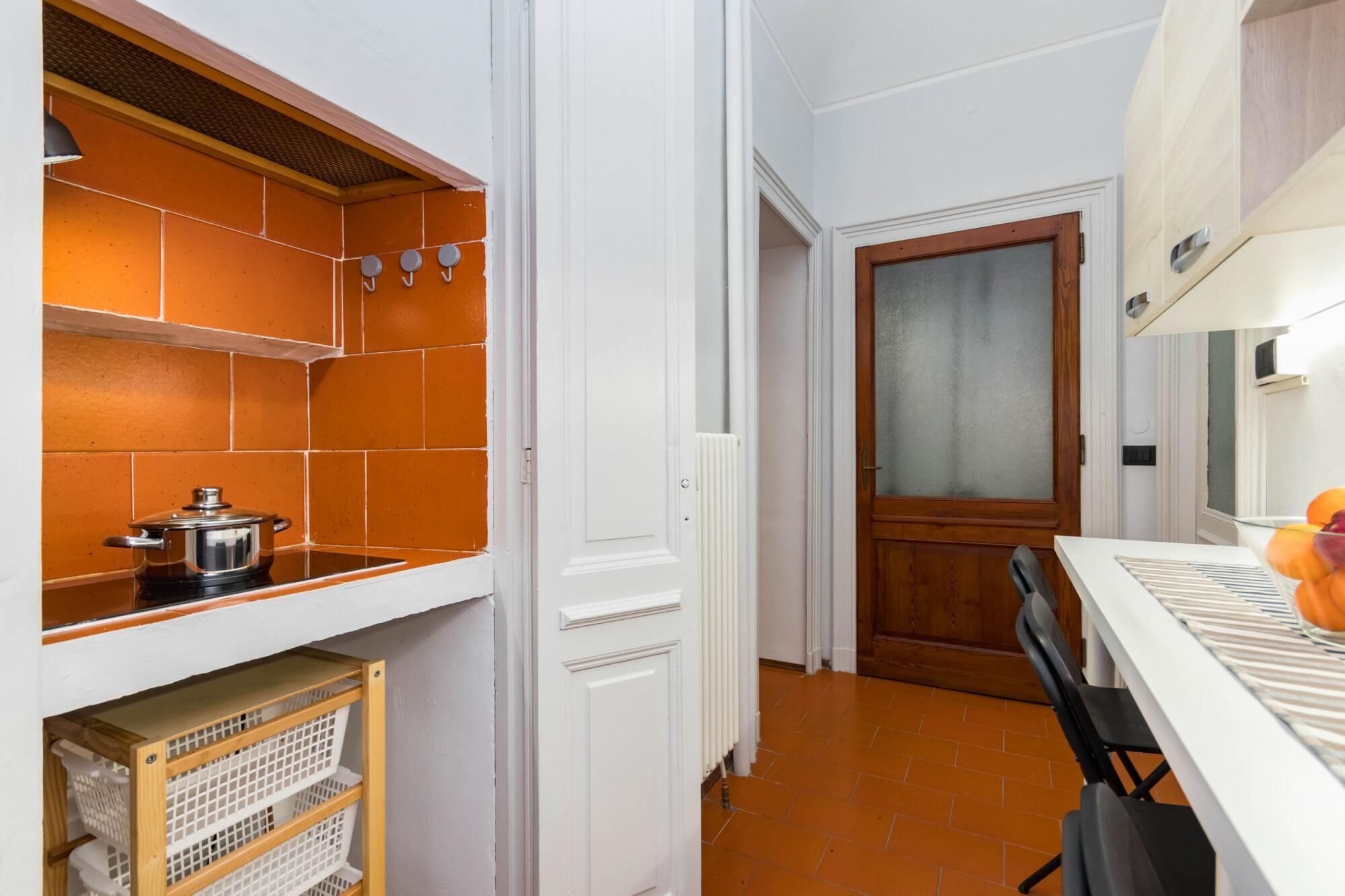 Et køkken med orange fliser, en hvid dør og et bord med stole.