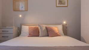 Una cama bien hecha con dos almohadas, una mesita de noche con una lámpara y dos cuadros en la pared.
