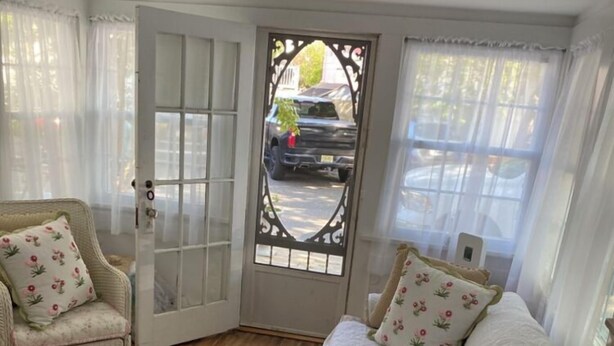A cozy room with a white sofa, two chairs, a wooden floor, and a decorative door with a view of the street. - Charming Beach Cottage,  Newly renovated. located in Ocean City Nj. (Ocean City)