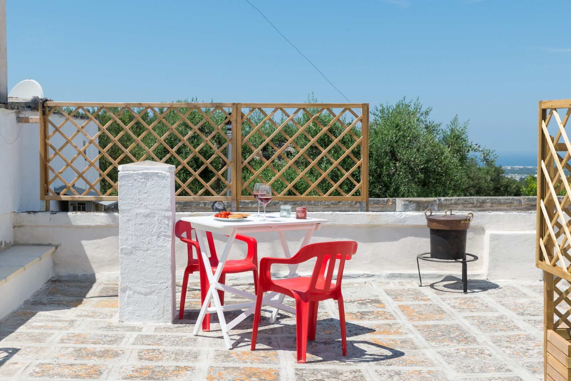 A rooftop terrace with a table and chairs, a potted plant, and a view of the sea.