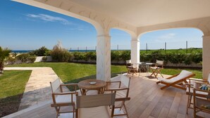 A covered patio with outdoor furniture, a view of the sea, and a well-maintained garden.