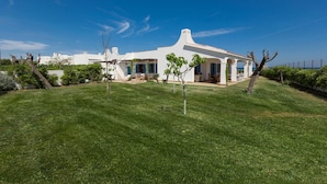 A white villa with a spacious lawn, a covered patio, and a clear blue sky.
