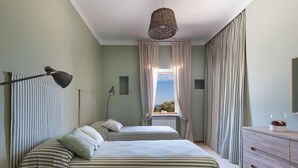 A bedroom with two beds, a dresser, a lamp, and a view of the sky through the window.
