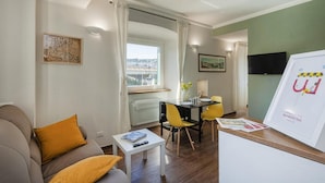 A modern living room with a sofa, a dining table with yellow chairs, a white coffee table, and a TV on the wall. - San Lorenzo View Apartment 5 by Wonderful Italy (Genoa)