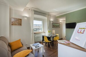 Una sala de estar moderna con un sofá, una mesa de comedor con sillas amarillas, una mesa de centro blanca y un televisor en la pared.