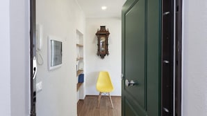 A narrow hallway with a green door, a wooden wall clock, a yellow chair, and a telephone. - San Lorenzo View Apartment 5 by Wonderful Italy (Genoa)