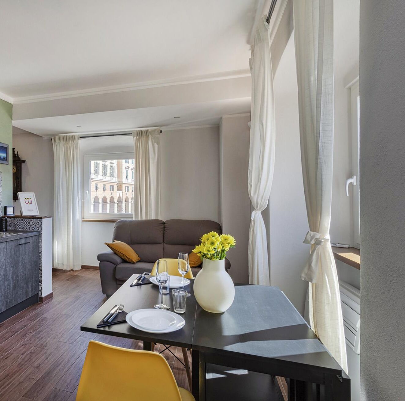 Ein modernes Hotelzimmer mit Essbereich, einer Couch und Blick auf Gebäude durch ein Fenster.