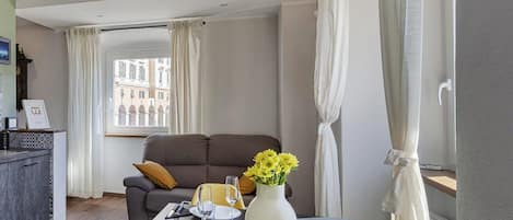 A modern hotel room with a dining area, a sofa, and a view of buildings through a window.