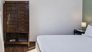 A bedroom with a bed, a wooden dresser with multiple drawers, a nightstand with a lamp, and a wall-mounted light fixture. - San Lorenzo View Apartment 5 by Wonderful Italy (Genoa)
