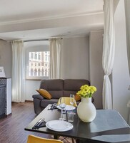 Una sala moderna con un sofá, una mesa de comedor para dos personas y un jarrón con flores amarillas.