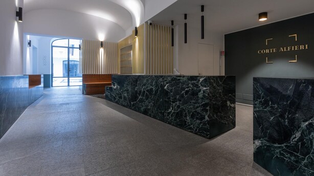 A modern reception area with a marble counter, a large window, and a wall-mounted sign reading "Corte Alfieri".