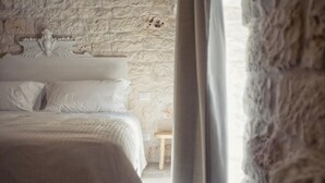 Ein Schlafzimmer mit einer Steinwand, einem Bett mit weißer Bettwäsche und einem hölzernen Hocker.