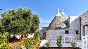 Ein Steinhaus mit einem spitzen Dach, ein Baum im Vordergrund und eine Terrasse mit weißer Möbel.