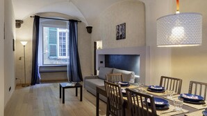 A modern living room with a sofa, dining table set for four, and a large window with curtains.