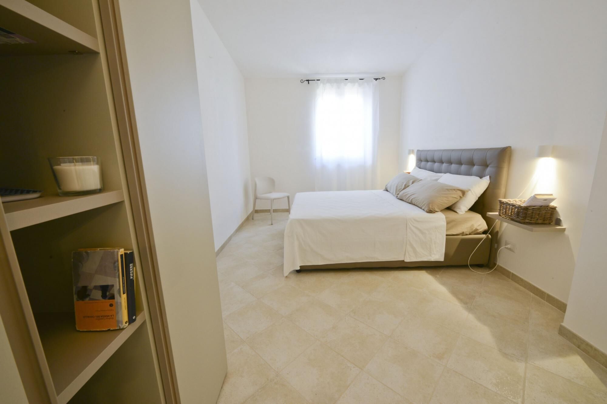 Une chambre à coucher avec un lit, une chaise, une étagère remplie de livres et une fenêtre avec des rideaux.