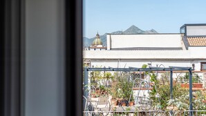 A view from a window overlooking a courtyard with potted plants, a metal pergola, and a building with a dome structure in the background.
