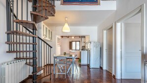 A modern kitchen with a central island, a dining area with a table and chairs, and a spiral staircase with a pendant light.
