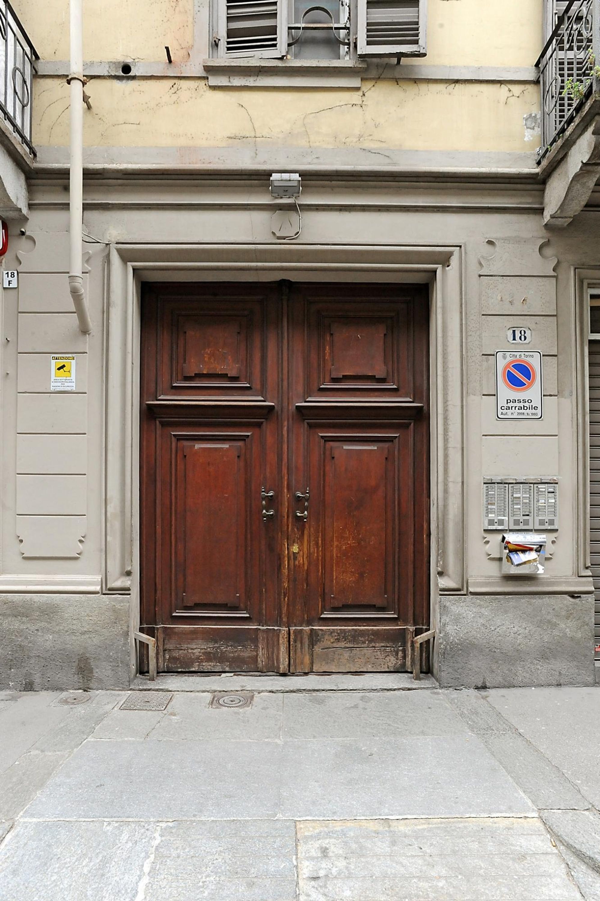 A double wooden door with a metal handle, set in a building with a light-colored facade and a small balcony above.