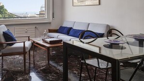 Una sala de estar moderna con sofá, sillas, una mesa de comedor y vistas a la ciudad a través de un ventanal amplio.