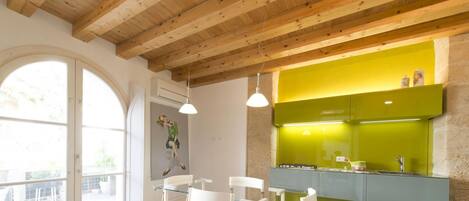 Una habitación con techo de madera, una pared verde decorativa, una zona de comedor con sillas blancas y una ventana con vistas.