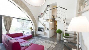 A modern living room with a pink sofa, a flat-screen TV, and a staircase leading to a second floor. - Luxury Gattopardo Loft - Lago Design by Wonderful Italy (Palermo)