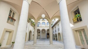 A spacious courtyard with a central open area, surrounded by columns and arches, leading to a staircase and a large windowed room. - Luxury Gattopardo Loft - Lago Design by Wonderful Italy (Palermo)