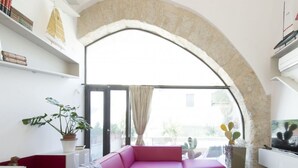 A modern living room with a large arched window, a pink sofa, a flat-screen TV, and a bookshelf. - Luxury Gattopardo Loft - Lago Design by Wonderful Italy (Palermo)