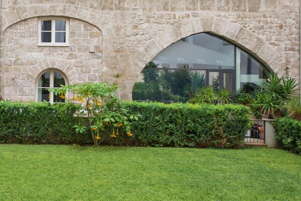 A stone building with a large arched window and a well-maintained hedge in front. - Luxury Gattopardo Loft - Lago Design by Wonderful Italy (Palermo)