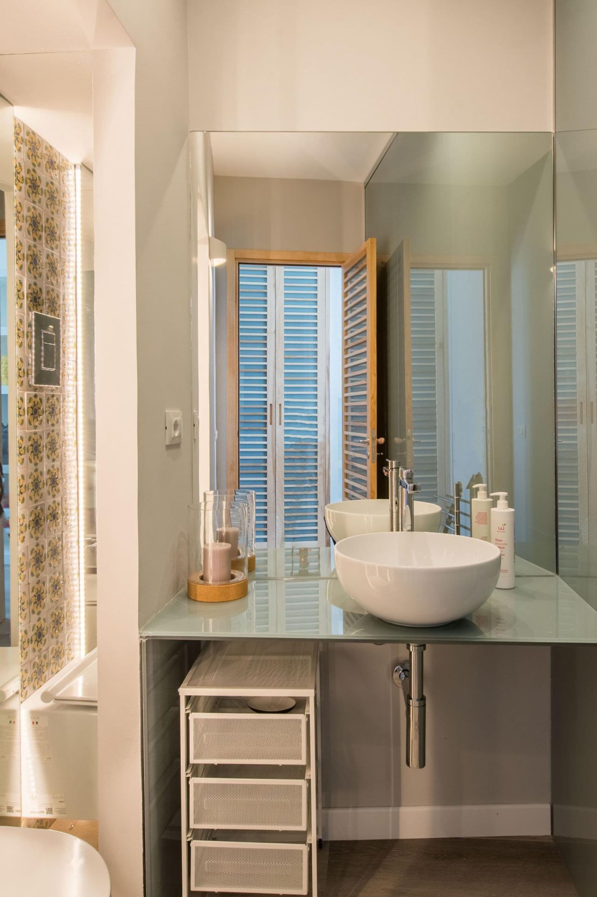 Un bagno moderno con uno specchio grande, un lavandino bianco e una cabina doccia in vetro.