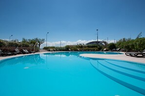 Ein klarer, blauer Swimmingpool mit Liegestühlen und einem modernen Gebäude im Hintergrund.