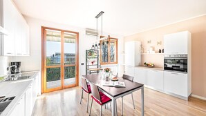 A modern kitchen with a dining area, featuring a large window, white cabinetry, and a built-in oven. - La Piopa 2 20 in Polpenazze del Garda (Polpenazze del Garda)