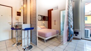 A bedroom with a bed, a small desk with a chair, a radiator, and a window with blinds. - Massarenti 14 a Porta S Vitale by Wonderful Italy (Bologna)