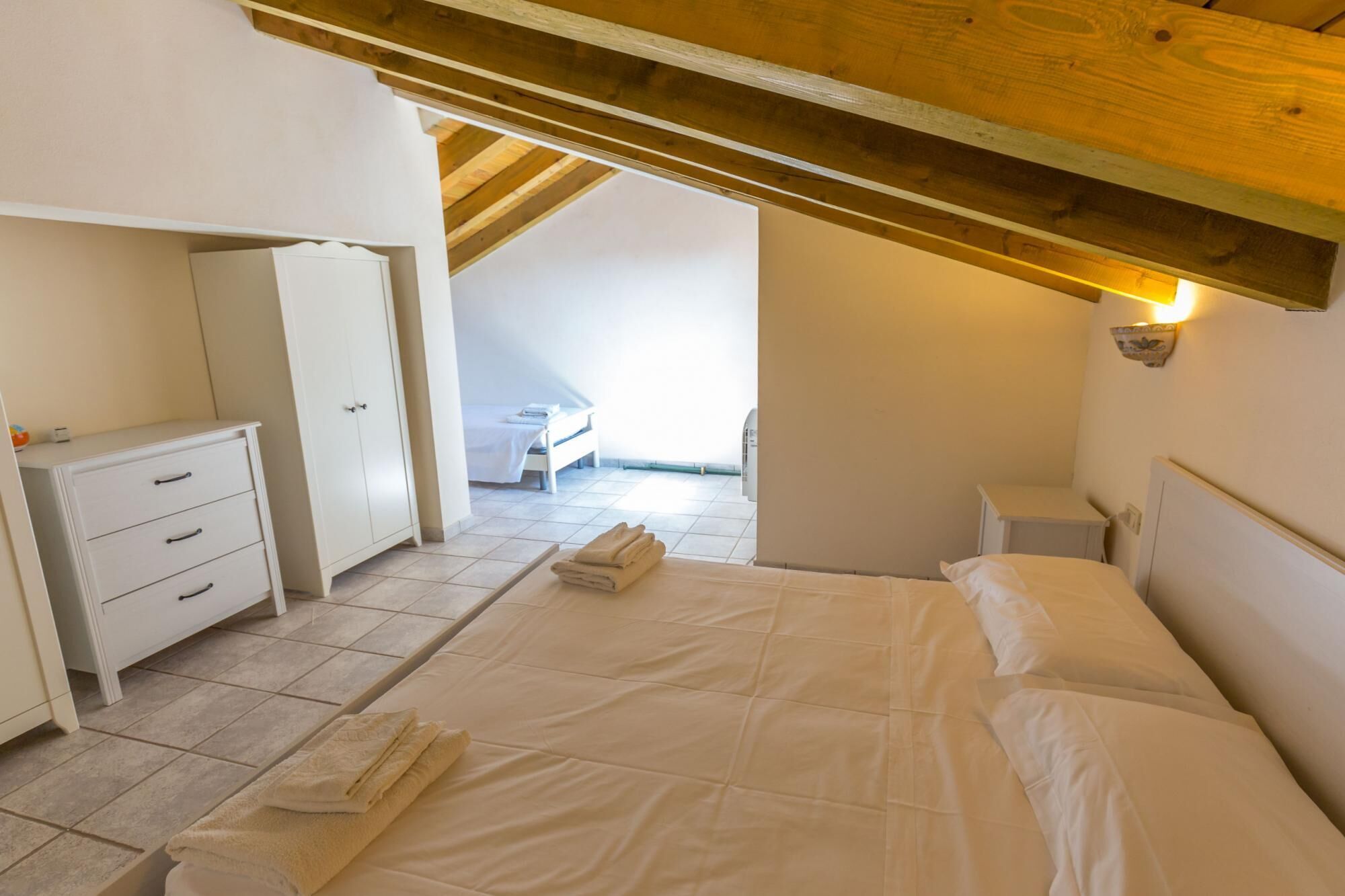 Ein Schlafzimmer mit einem großen Bett, einem Kleiderschrank, einem Nachttisch und Blick auf einen Balkon.