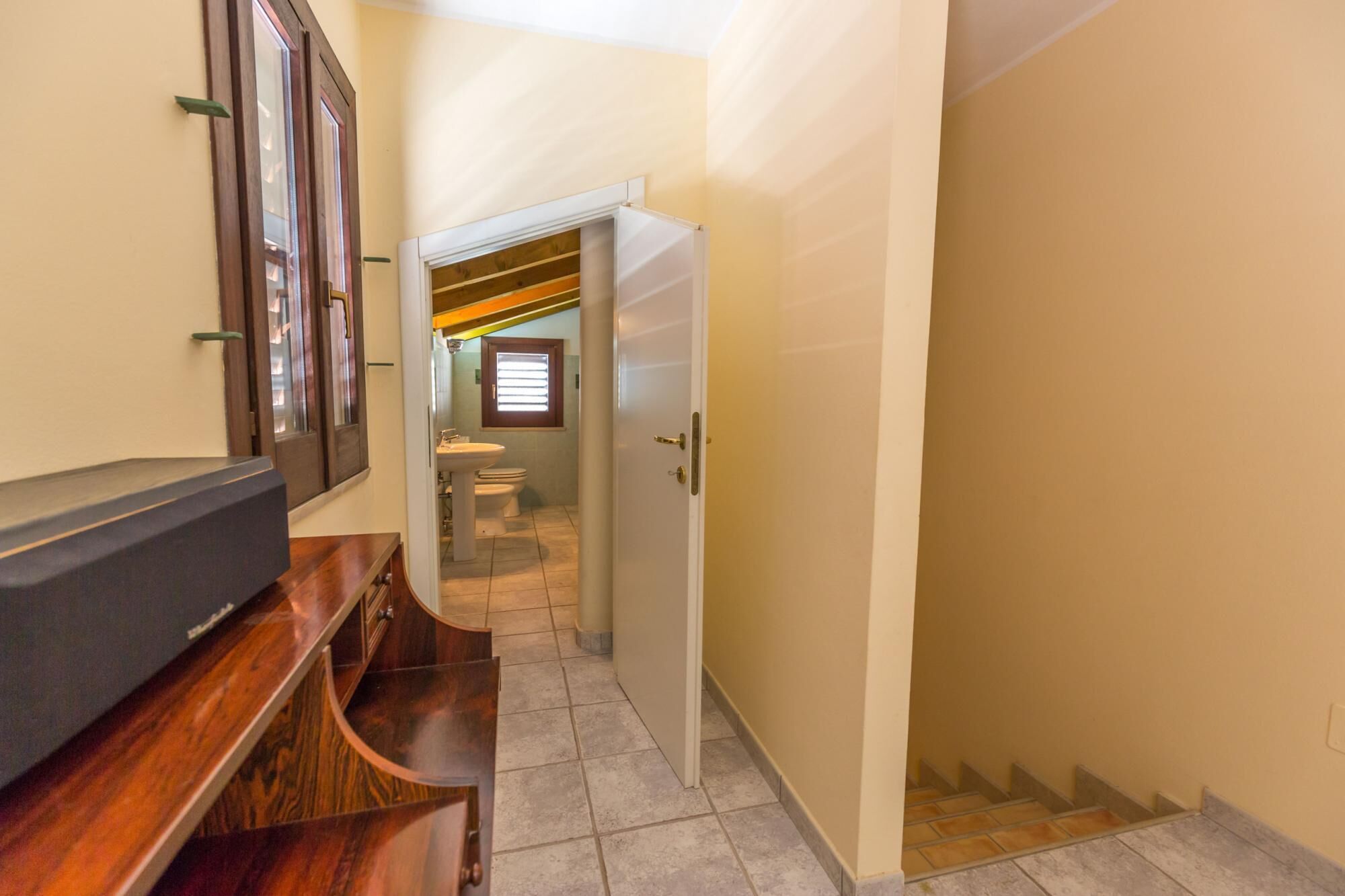 A narrow hallway with a wooden desk and a white door leading to a bathroom.