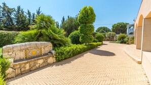 A paved pathway leading to a building with a stone wall and a decorative tile. - Villa Arenella con Piscina by Wonderful Italy (Syracuse)