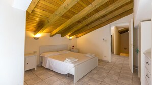 A bedroom with a sloped ceiling, a bed, bedside tables, and a door leading to a bathroom. - Villa Arenella con Piscina by Wonderful Italy (Syracuse)