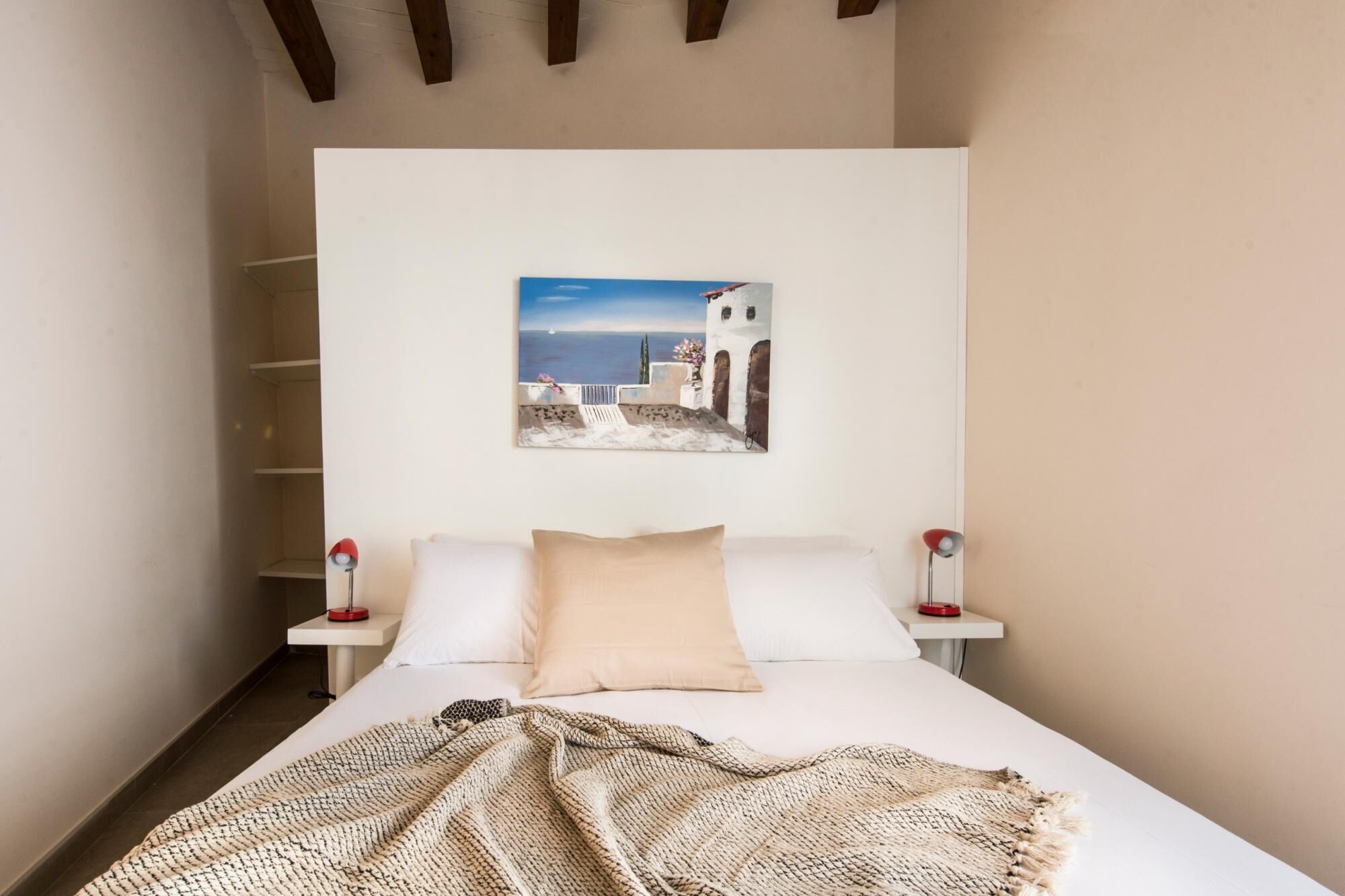 Un dormitorio con cama, un cuadro de una escena costera y lámparas de noche.
