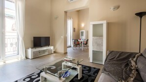 A living room with a TV, glass coffee table, sofa, and a dining area with chairs and a table.