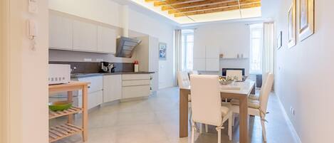 A modern kitchen with white cabinets, a wooden ceiling, and a dining area with a table and chairs.