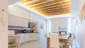 A modern kitchen with white cabinets, a wooden ceiling, and a dining area with white chairs and a table.