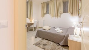 A bedroom with a bed, bedside table, lamp, and a desk with chair.