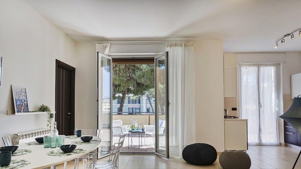Une cuisine moderne dotée d’une cuisinière intégrée, un coin repas avec une table dressée pour deux personnes, et une porte-fenêtre coulissante donnant sur une terrasse extérieure.