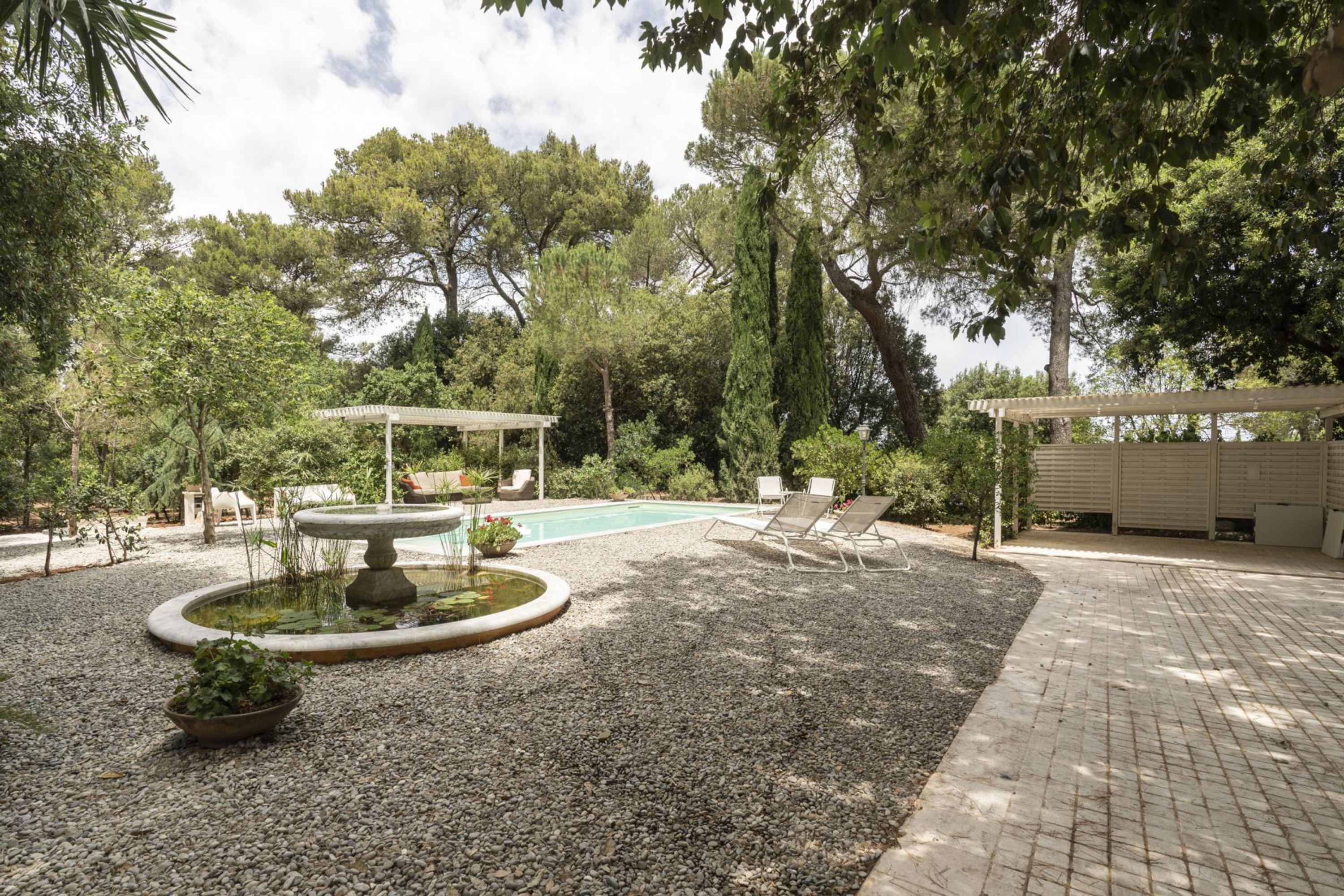 A garden with a swimming pool, a pergola, and lounge chairs.