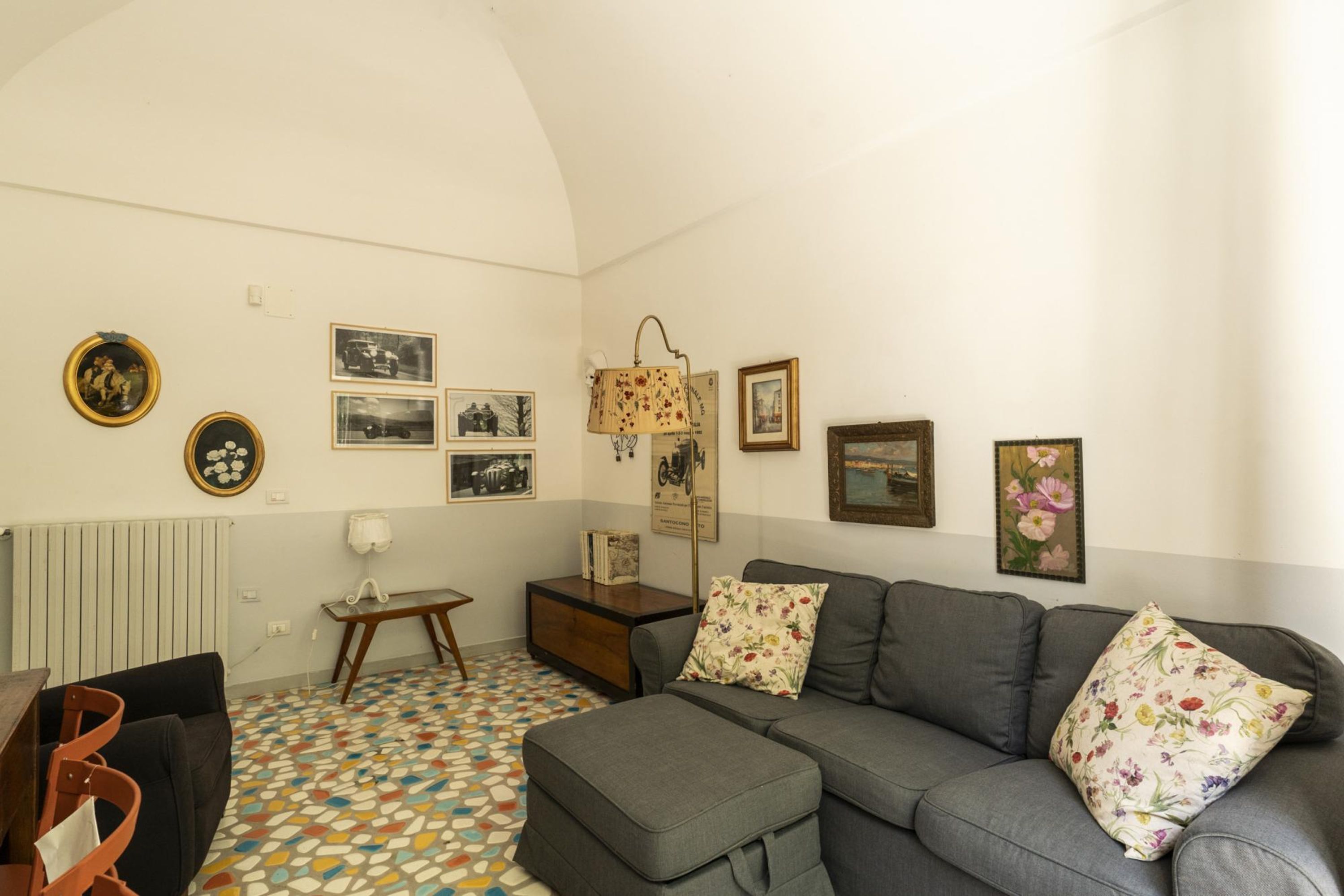 A living room with a gray sofa, floral cushions, a patterned floor, and wall-mounted pictures.