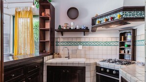 A compact kitchen with a sink, stove, and shelves with kitchenware. - Villa Amun con Giardino by Wonderful Italy (Riposto)