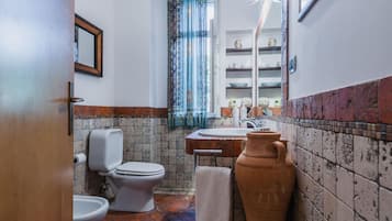 Ein Badezimmer mit Toilette, Bidet und Waschbecken. Ein Handtuchhalter und ein Spiegel befinden sich über dem Waschbecken.